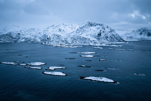 Aerial view of snow laden peaks meet the frigid waters speckled with rocky islands a symphony of cold blues and whites Hamn Troms Norway. Aerial view of snow laden peaks meet the frigid waters speckled with rocky islands a symphony of cold blues and whites Hamn Troms Norway.