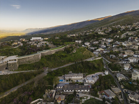 Aerial view of Gjirokaster Fortress with its historic stone walls surrounded by traditional houses and lush green hillsides during the golden hour in Gjirokaster Gjirokaster County Albania. Aerial view of Gjirokaster Fortress with its historic stone walls surrounded by traditional houses and lush green hillsides during the golden hour in Gjirokaster Gjirokaster County Albania.