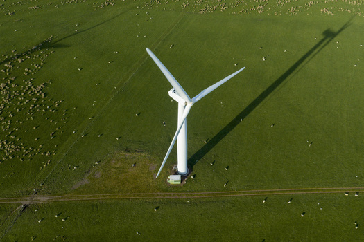 Aerial view of a large white wind turbine casting a long shadow across a green field with grazing sheep in Scotland United Kingdom. Aerial view of a large white wind turbine casting a long shadow across a green field with grazing sheep in Scotland United Kingdom.