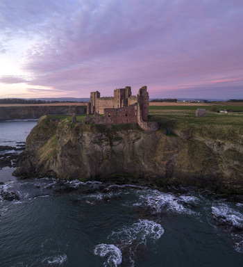 Aerial view of Tantallon Castle on a rugged cliff overlooking the sea under a purple sunset sky North Berwick Scotland United Kingdom.