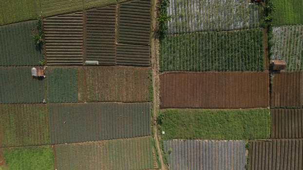 Aerial view of geometric agricultural fields with various crops brown soil plots and small farm huts in Sukabumi West Java Indonesia. Aerial view of geometric agricultural fields with various crops brown soil plots and small farm huts in Sukabumi West Java Indonesia.