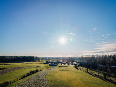 Valmiera Latvia 18 November 2025 Aerial view of a golf club building and course on a frosty morning with green fairways surrounding trees and bright sunlight.