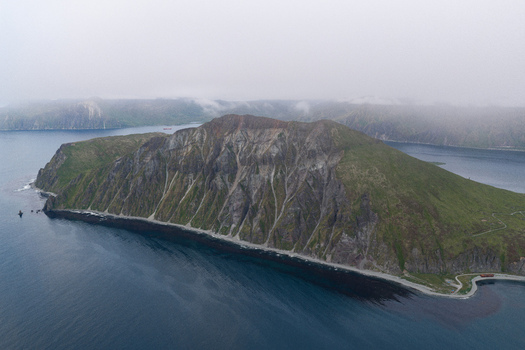 Aerial view of Mount Ballyhoo with rugged green slopes rocky cliffs and dark volcanic sand beaches surrounded by the deep blue waters of the Bering Sea in Unalaska Alaska United States.