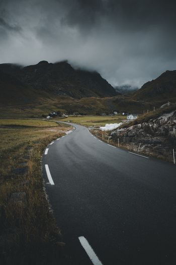View of a winding asphalt road leading through a dramatic mountainous landscape under a moody overcast sky near Haukland Beach in Leknes Nordland Norway. View of a winding asphalt road leading through a dramatic mountainous landscape under a moody overcast sky near Haukland Beach in Leknes Nordland Norway.