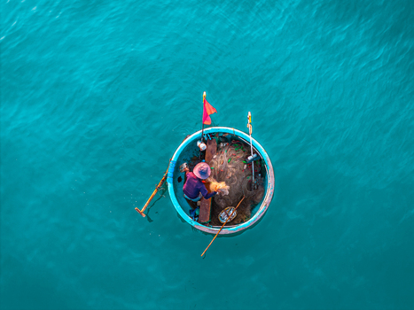 Aerial view of a fisherman working in a traditional round basket boat with fishing nets and a red flag on turquoise water in Vietnam. Aerial view of a fisherman working in a traditional round basket boat with fishing nets and a red flag on turquoise water in Vietnam.