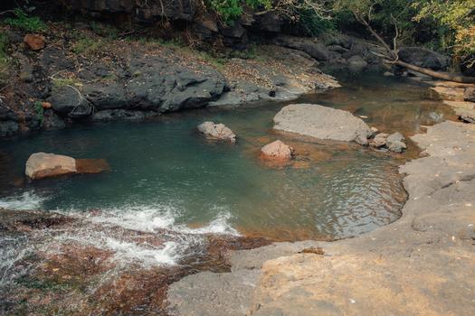 View of a serene stream flowing between rocky banks with sunlight glinting on the water s surface creating a tranquil scene Chiplun Maharashtra India.