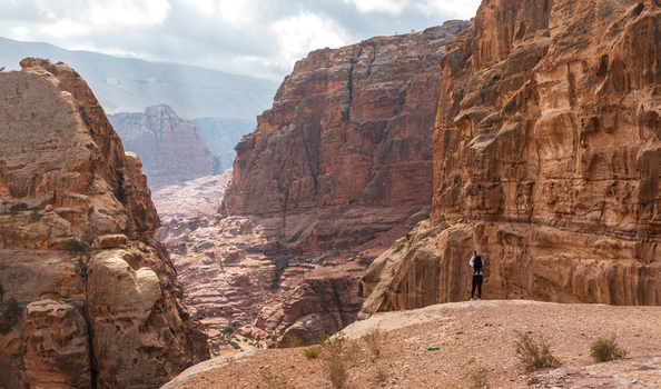 View of a hiker standing on a rocky ledge overlooking the deep rugged sandstone canyon of Wadi Musa Ma an Governorate Jordan. View of a hiker standing on a rocky ledge overlooking the deep rugged sandstone canyon of Wadi Musa Ma an Governorate Jordan.