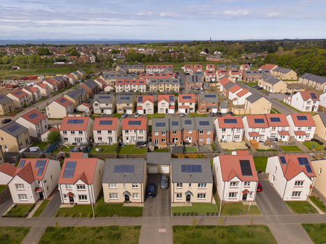 Aerial view of a modern residential neighborhood featuring solar panels on rooftops and lush green trees in Edinburgh Scotland United Kingdom.
