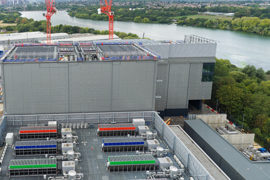 Aerial view of a large data center under construction featuring industrial cooling units on the roof red cranes and a river in the background in the United Kingdom.