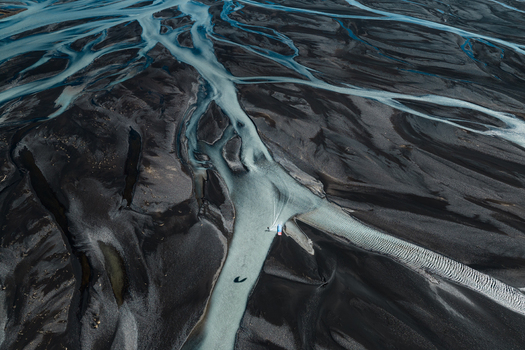 Aerial view of a braided glacial river flowing through dark volcanic sand in the rugged landscape of Skaftarhreppur Iceland.