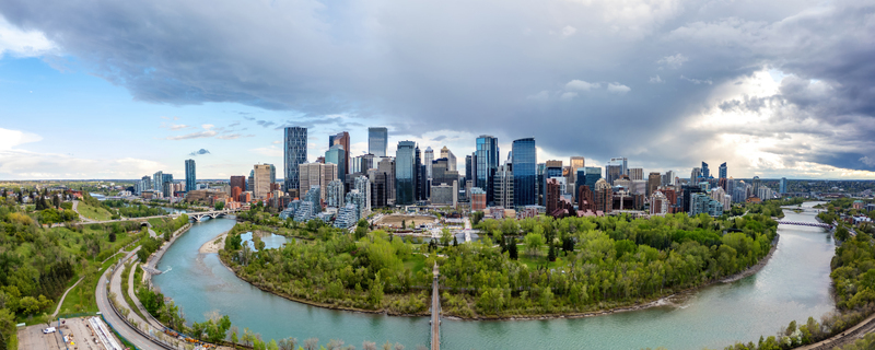 Aerial view of the Calgary skyline rising above the Bow River with lush green trees and dramatic storm clouds in the background in Calgary Alberta Canada.
