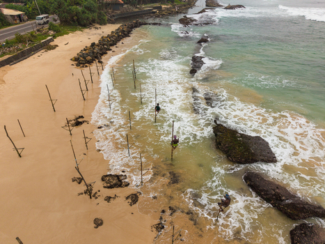 Aerial view of stilt fishermen on traditional wooden poles in the turquoise ocean waves along the sandy beach Koggala Southern Province Sri Lanka. Aerial view of stilt fishermen on traditional wooden poles in the turquoise ocean waves along the sandy beach Koggala Southern Province Sri Lanka.