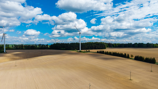 Aerial view of wind turbines standing in vast agricultural fields near a dense forest under a cloudy blue sky in Gruna Pardubicky kraj Czechia. Aerial view of wind turbines standing in vast agricultural fields near a dense forest under a cloudy blue sky in Gruna Pardubicky kraj Czechia.