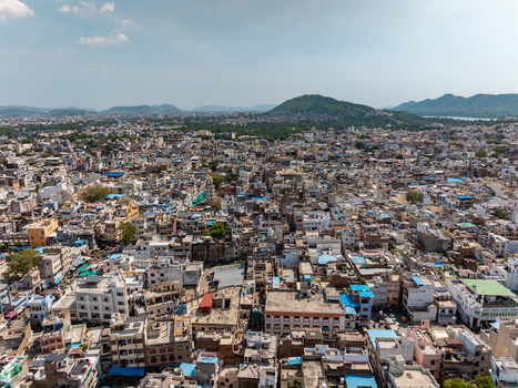 Aerial view of the dense urban landscape featuring historic buildings rooftops and surrounding hills under a clear sky in Udaipur Rajasthan India.