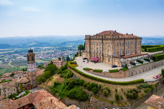 Aerial view of the historic Castello di Guarene with its grand brick facade and clock tower overlooking the terracotta rooftops and rolling hills of Guarene Piedmont Italy. Aerial view of the historic Castello di Guarene with its grand brick facade and clock tower overlooking the terracotta rooftops and rolling hills of Guarene Piedmont Italy.