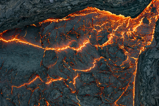 Aerial view of fiery lava flows contrasting against the dark rugged volcanic landscape Grindav&iacute;kurb&aelig;r Iceland.