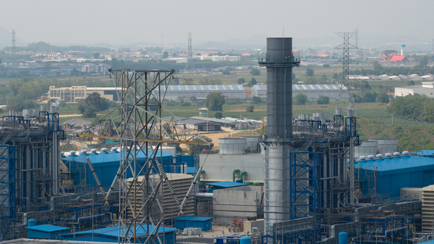 Aerial view of the GPD industrial power plant featuring blue factory buildings tall exhaust stacks and high voltage electricity pylons under a hazy sky in Map Yang Phon Rayong Thailand.