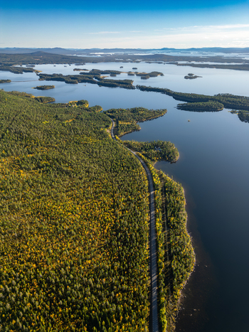 Aerial view of Galtispuoda featuring a road winding through dense forests alongside a vast lake with islands under a clear sky in Arjeplog Norrbotten County Sweden.