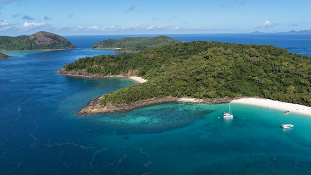 Aerial view of Whitehaven Beach with turquoise waters white sand and boats anchored near lush green islands in Whitsundays Queensland Australia.
