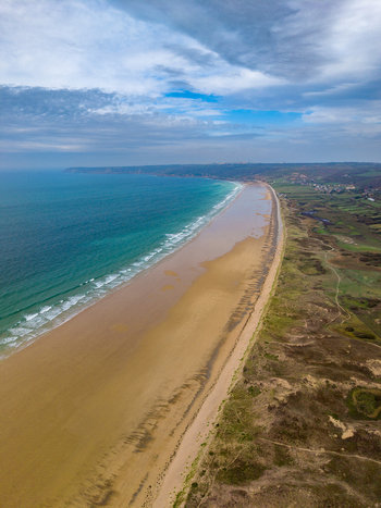 Aerial view of Dunes de Biville featuring the expansive sandy beach turquoise ocean waves and rolling coastal dunes under a cloudy sky in La Hague Normandie France.