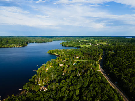 Aerial view of Commanda Lake surrounded by lush green forests a winding road and calm blue waters under a bright sky in Restoule Ontario Canada. Aerial view of Commanda Lake surrounded by lush green forests a winding road and calm blue waters under a bright sky in Restoule Ontario Canada.