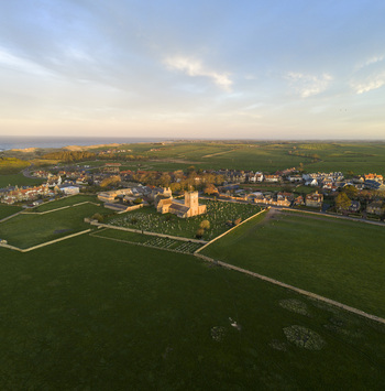 Aerial view of St Aidan s Church surrounded by a historic graveyard and lush green fields under a soft evening sky in Bamburgh England United Kingdom. Aerial view of St Aidan s Church surrounded by a historic graveyard and lush green fields under a soft evening sky in Bamburgh England United Kingdom.