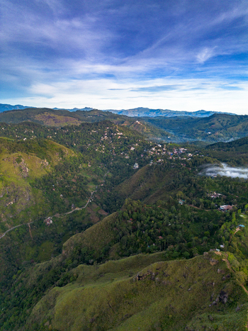 Aerial view of Little Adam s Peak surrounded by lush green mountains rolling hills and dense forests under a blue sky in Badulla Uva Province Sri Lanka. Aerial view of Little Adam s Peak surrounded by lush green mountains rolling hills and dense forests under a blue sky in Badulla Uva Province Sri Lanka.