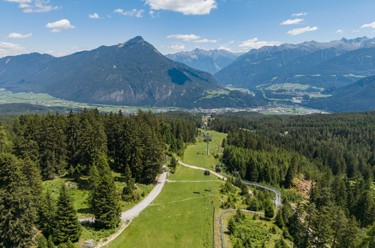 Aerial view of the Imst mountain resort with a cable car line green alpine meadows dense coniferous forests and panoramic mountain peaks in Imst Tyrol Austria.