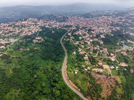 Aerial view of a winding road cutting through lush green hills and a hillside town in Ghana. Aerial view of a winding road cutting through lush green hills and a hillside town in Ghana.