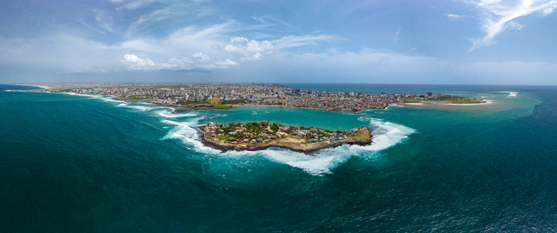 Aerial view of Ngor Island surrounded by turquoise ocean waves with the city skyline in the background in Dakar Dakar Region Senegal.