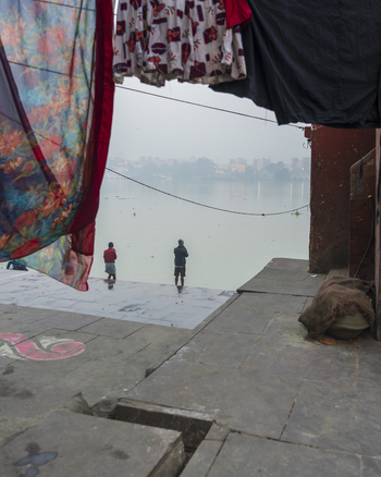 View of two figures standing on a concrete platform by the misty river framed by colorful fabrics drying overhead in Kolkata West Bengal India. View of two figures standing on a concrete platform by the misty river framed by colorful fabrics drying overhead in Kolkata West Bengal India.