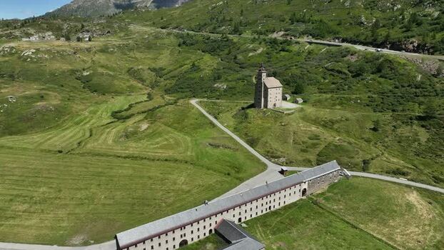 Aerial view of the historic Alter Spittel building at Simplon Pass surrounded by green alpine slopes and winding mountain roads in Simplon Valais Switzerland.
