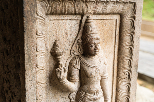 View of an intricate ancient stone carving of a deity holding a lotus flower on a temple pillar Kandy Central Province Sri Lanka. View of an intricate ancient stone carving of a deity holding a lotus flower on a temple pillar Kandy Central Province Sri Lanka.