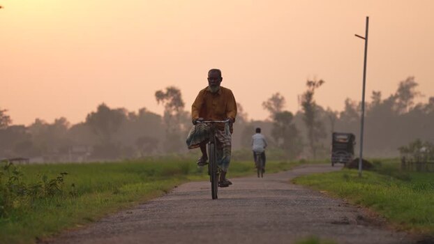View of a man riding a bicycle on a rural road Bangladesh.