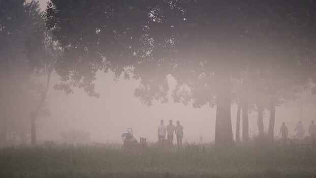 View of people standing in thick fog under trees Bangladesh.