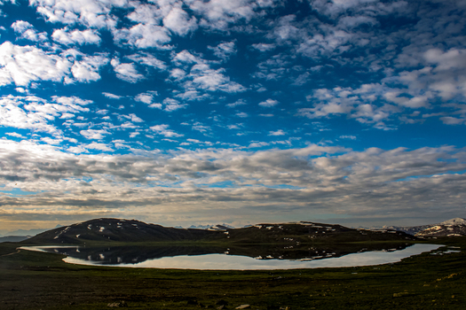 View of Sheosar Lake with its calm waters reflecting the dramatic cloudy sky and surrounding snow capped mountains in the Deosai National Park area of Skardu Pakistan. View of Sheosar Lake with its calm waters reflecting the dramatic cloudy sky and surrounding snow capped mountains in the Deosai National Park area of Skardu Pakistan.