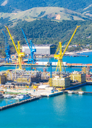 Aerial view of the industrial shipyard with large yellow and blue cranes cargo containers and ships docked along the waterfront in Angra dos Reis Rio de Janeiro Brazil.