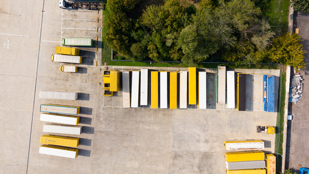 Aerial view of rows of dry van trailers parked in a logistics yard with concrete pavement and surrounding trees in Milan Lombardy Italy. Aerial view of rows of dry van trailers parked in a logistics yard with concrete pavement and surrounding trees in Milan Lombardy Italy.