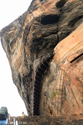 View of the massive granite rock face and metal staircases of the Sigiriya Rock Fortress with tourists climbing the stone steps Sigiriya Central Province Sri Lanka. View of the massive granite rock face and metal staircases of the Sigiriya Rock Fortress with tourists climbing the stone steps Sigiriya Central Province Sri Lanka.