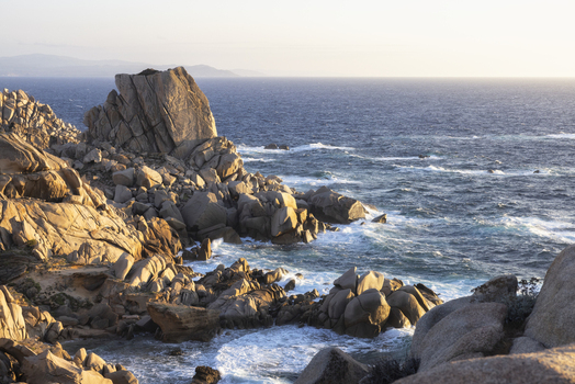 View of the rugged granite rock formations of Capo Testa with crashing waves and golden sunlight over the Mediterranean Sea Capo Testa Sardegna Italy. View of the rugged granite rock formations of Capo Testa with crashing waves and golden sunlight over the Mediterranean Sea Capo Testa Sardegna Italy.
