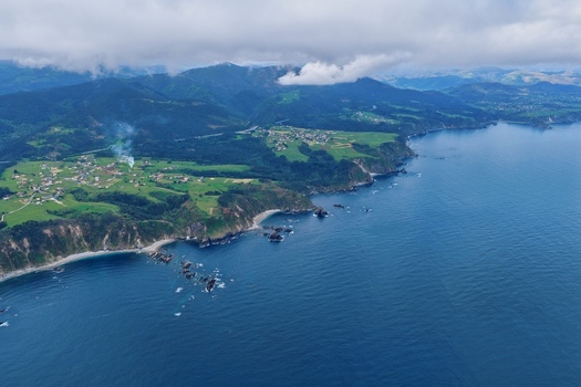Aerial view of the Silence Beach Viewpoint and the rugged coastline with steep cliffs green meadows and small coastal villages under a cloudy sky in Cudillero Asturias Spain.