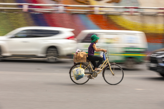 View of a person wearing a green hat riding a bicycle loaded with goods through busy traffic in Hanoi Ha Noi Vietnam.