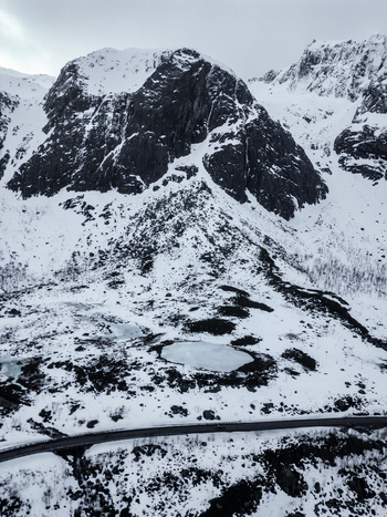 Aerial view of the snowy peaks of Grotfjord with a frozen pond and a winding road in Tromvik Troms Norway. Aerial view of the snowy peaks of Grotfjord with a frozen pond and a winding road in Tromvik Troms Norway.