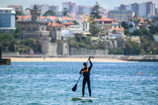 Cascais e Estoril Portugal 13 May 2026 View of a man stand up paddleboarding on calm waters with the historic Palacio do Conde de Castro Guimaraes and city skyline in the background.