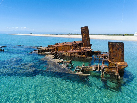 Aerial view of the rusty Shipwreck Epanomi submerged in turquoise shallow waters along a sandy beach under a clear blue sky Epanomi Greece.