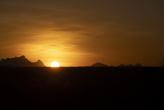 View of the sun setting behind silhouetted mountain peaks under a vibrant golden sky in Sololo Marsabit County Kenya.
