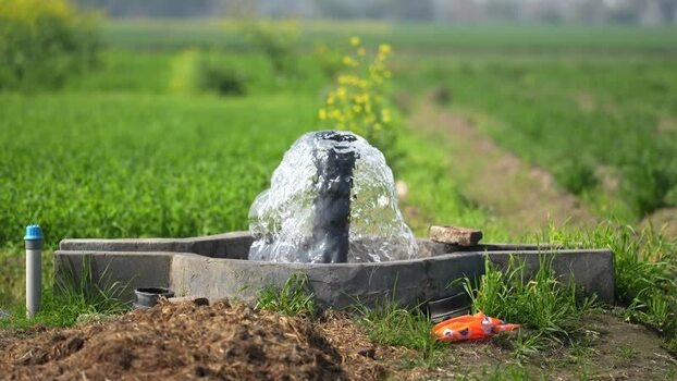 View of a water pump gushing in a green field India.