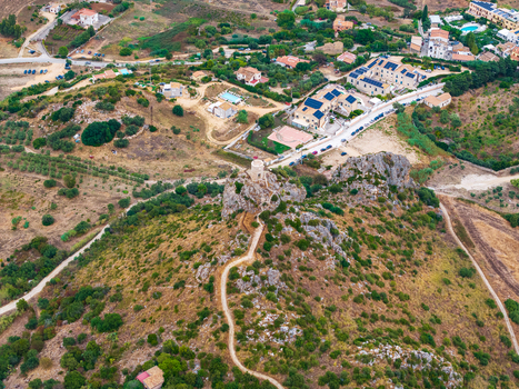Aerial view of a historic stone tower perched on a rocky hilltop with a winding path surrounded by Mediterranean landscape and residential buildings in Palermo Sicily Italy. Aerial view of a historic stone tower perched on a rocky hilltop with a winding path surrounded by Mediterranean landscape and residential buildings in Palermo Sicily Italy.
