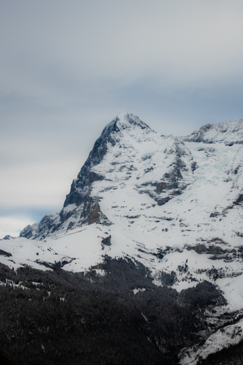 View of snow capped mountain rises majestically against a cloudy sky its rocky face partially covered in white creating a stark contrast Murren Switzerland. View of snow capped mountain rises majestically against a cloudy sky its rocky face partially covered in white creating a stark contrast Murren Switzerland.