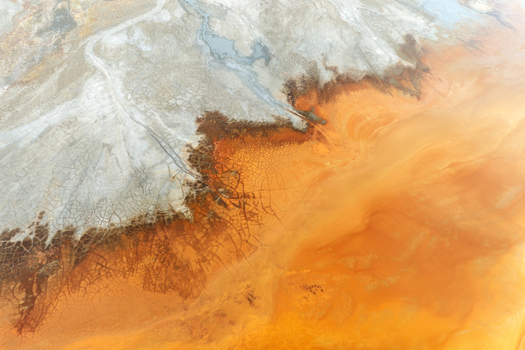 Aerial view of the Minas de Riotinto showing vibrant orange acidic water and cracked earth patterns with white mineral deposits in Minas de Riotinto Andalusia Spain.